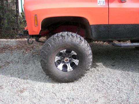 1990 Chevrolet Suburban - Close-up of the front fender and wheel of an orange pickup truck, showing off-road modifications.