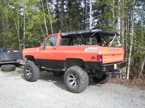 1990 Chevrolet Suburban - This lifted SUV features an 'Offroad Attitude' decal and a removable soft top, parked outdoors.