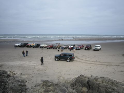 1996 Ford Bronco - Several SUVs and trucks are gathered on a beach near the ocean.