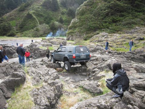 1996 Ford Bronco - SUV navigates rocky terrain near the coast, with spectators watching.