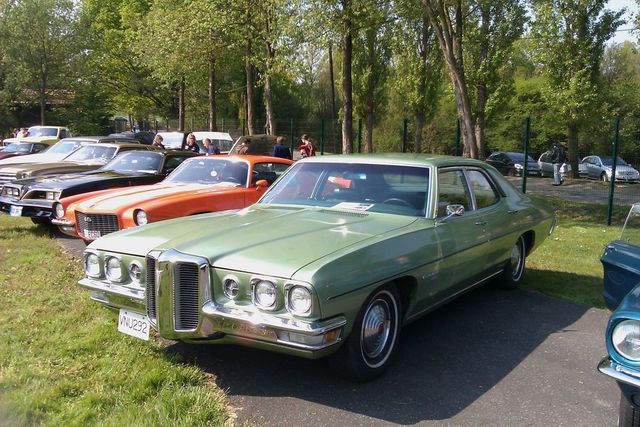 Green 1970s Pontiac sedan parked in a lot with other cars