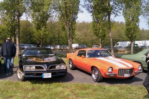 1991 Ford LTD Crown Victoria - Two iconic American muscle cars, a black Pontiac Firebird Trans Am and an orange Chevrolet Camaro, are displayed outdoors.