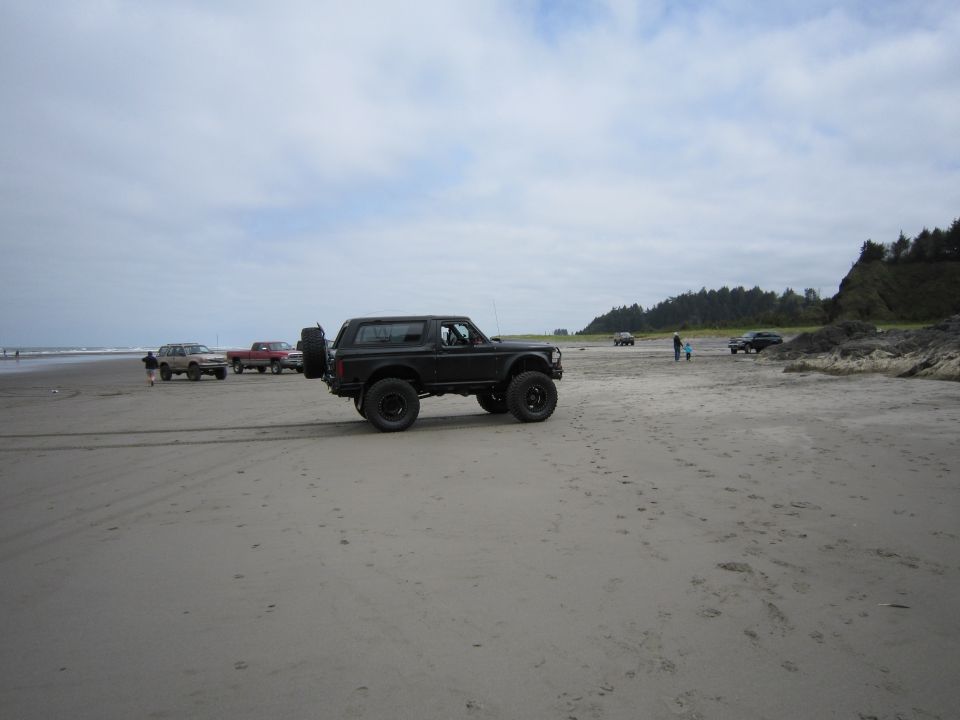 Black 1996 Ford Bronco on a sandy beach with other vehicles in the background