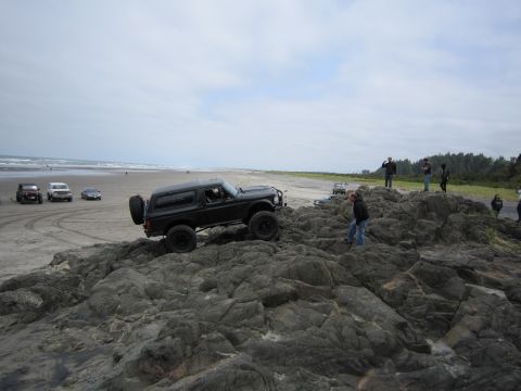1996 Ford Bronco - A group of off-road vehicles navigate a rocky shoreline under a cloudy sky.