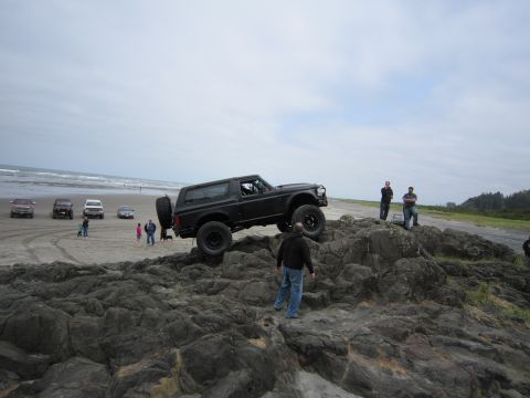 1996 Ford Bronco - Several vehicles are parked on the beach while one Bronco attempts to navigate rocky terrain.