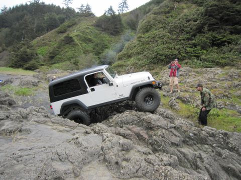 1996 Ford Bronco - A white Jeep Wrangler navigates a rocky coastal path with two people observing.