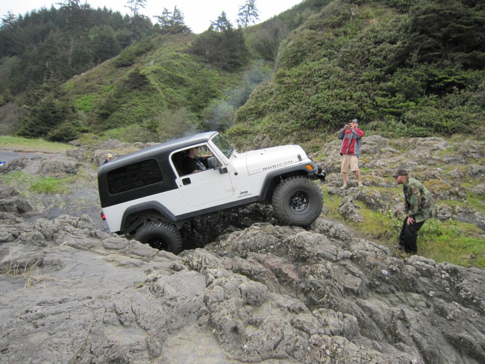White Jeep Wrangler Rubicon driving over rocks on a coastal trail