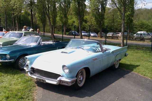 Light blue 1957 Ford Thunderbird convertible parked next to a teal 1967 Ford Mustang convertible