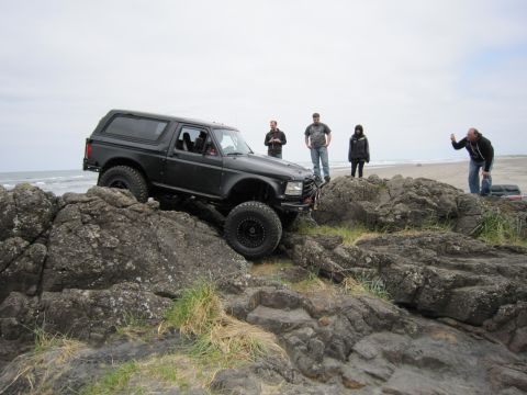 1996 Ford Bronco - A modified black Ford Bronco navigates a rocky coastal terrain with several onlookers observing the off-road activity.