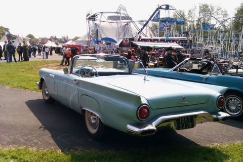 1991 Ford LTD Crown Victoria - A light blue 1957 Ford Thunderbird convertible is parked at an outdoor event with a roller coaster in the background.
