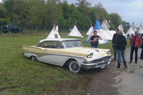 1991 Ford LTD Crown Victoria - A classic 1957 Ford Fairlane 500 hardtop coupe is parked on grass near teepees and people.