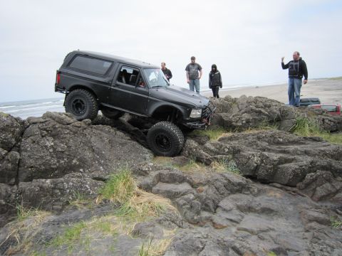 1996 Ford Bronco - 1996 Ford Bronco navigates rocky terrain by the ocean with onlookers present.