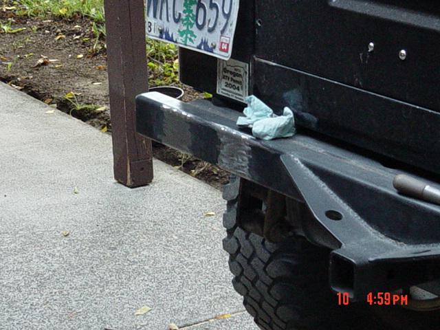 Heavy steel rear bumper and tow shackle on a lifted truck parked at a curb with rag draped over it