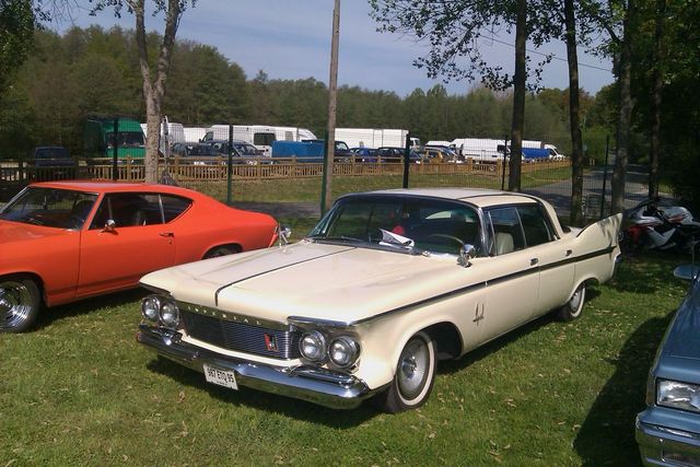 Cream-colored 1960 Chrysler Imperial sedan parked on grass next to an orange car