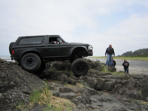 1996 Ford Bronco - A modified 1996 Ford Bronco navigates a rocky coastal terrain with people watching.