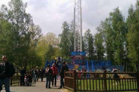 1991 Ford LTD Crown Victoria - A busy amusement park features a prominent drop tower ride, surrounded by trees and park-goers enjoying the day.