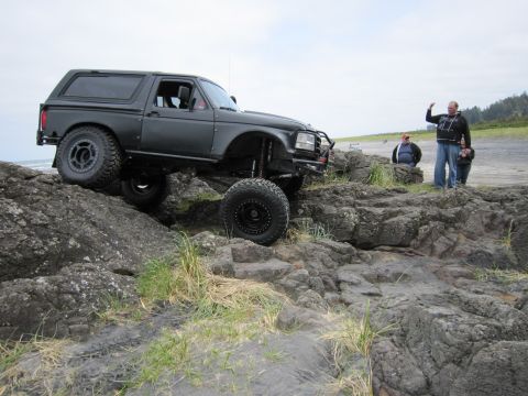 1996 Ford Bronco - A modified SUV navigates a rocky coastal terrain with people watching in the background.
