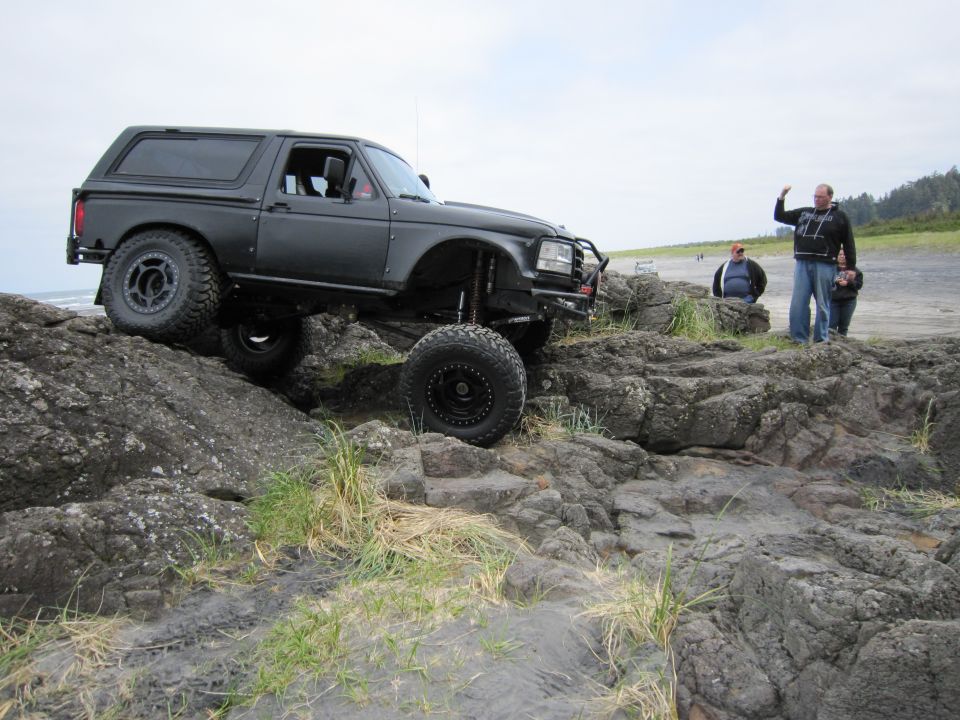 Black SUV with large tires climbing over rocks on a beach