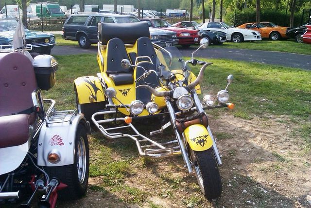 Yellow trike motorcycle with two seats and bull horns on the front, parked next to another trike