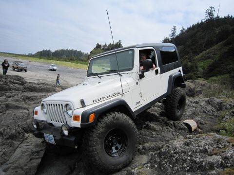 1996 Ford Bronco - A white Jeep Wrangler Rubicon navigates a rocky coastal path with other vehicles in the background.