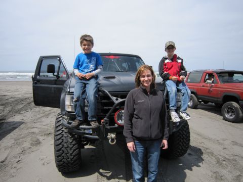 1996 Ford Bronco - A family poses with a heavily modified black truck on a sandy beach, with the ocean visible behind them.