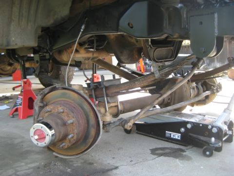 1994 Ford Bronco - Close-up view of the rear axle, leaf springs, and brake assembly of a vehicle undergoing maintenance.