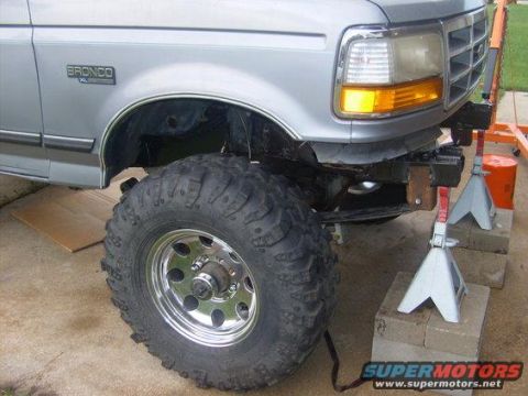 1994 Ford Bronco - Silver Ford Bronco with large tires on jack stands, front fender and bumper removed, revealing its chassis.
