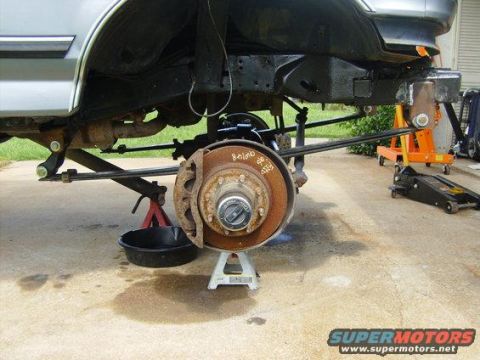 1994 Ford Bronco - Close-up view of a vehicle's suspension and brake components, supported by jack stands, with a Supermotors watermark visible.