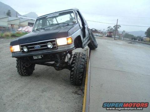 1994 Ford Bronco - This heavily modified Ford Bronco is shown with its front passenger side tire on a curb, highlighting its off-road capabilities.
