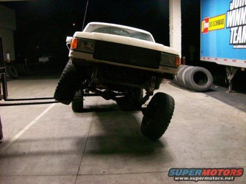 1994 Ford Bronco - A white Ford Bronco is lifted by a forklift, showing its front end and large tires.