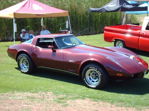 1992 Ford Bronco — Maroon 1975 Chevrolet Corvette parked on grass with a red pickup truck behind it