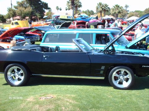 1992 Ford Bronco - A black convertible with custom blue flame graphics and chrome wheels is displayed at a car show, with other vehicles visible in the backgr…