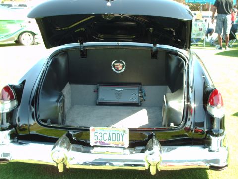 1992 Ford Bronco - The trunk of a black 1953 Cadillac reveals an amplifier and custom interior, with another car visible in the background.