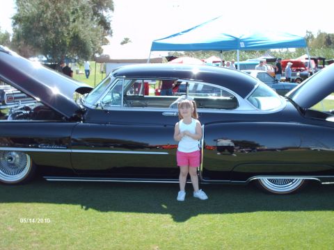1992 Ford Bronco - A young girl poses next to a classic black coupe with its hood open at a car show.