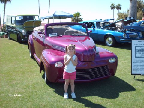 1992 Ford Bronco - A young girl poses in front of a custom purple convertible at a car show, with other vehicles and a display sign in the background.