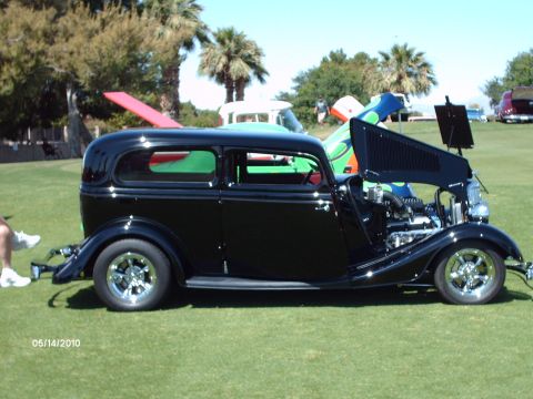 Black sedan hot rod with hood open, chrome wheels, on grass