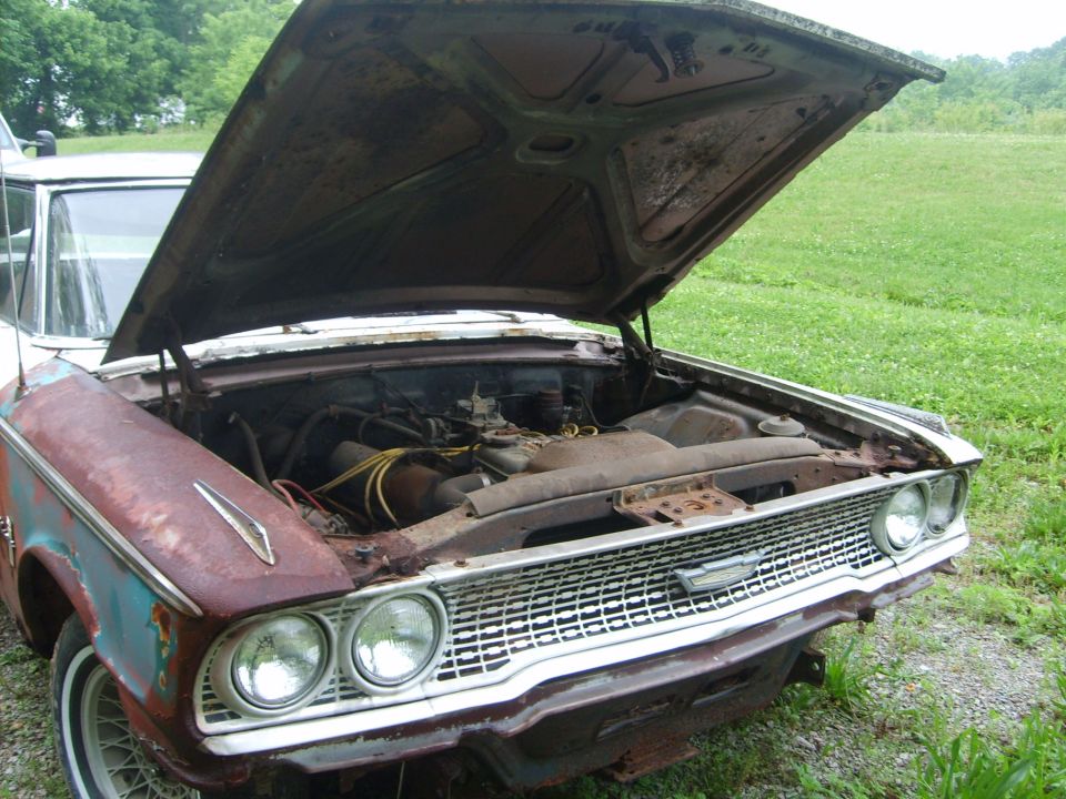 rusty car with hood up, showing engine and front grille. Looks like a 1961 model