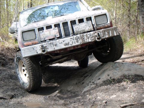 1998 Jeep Cherokee - A muddy 1997 Jeep Cherokee navigates a rocky trail, with its front tires climbing over an obstacle.