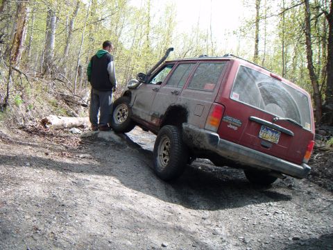 1998 Jeep Cherokee - A red Jeep Cherokee navigates a challenging off-road trail, tilted on a steep incline.