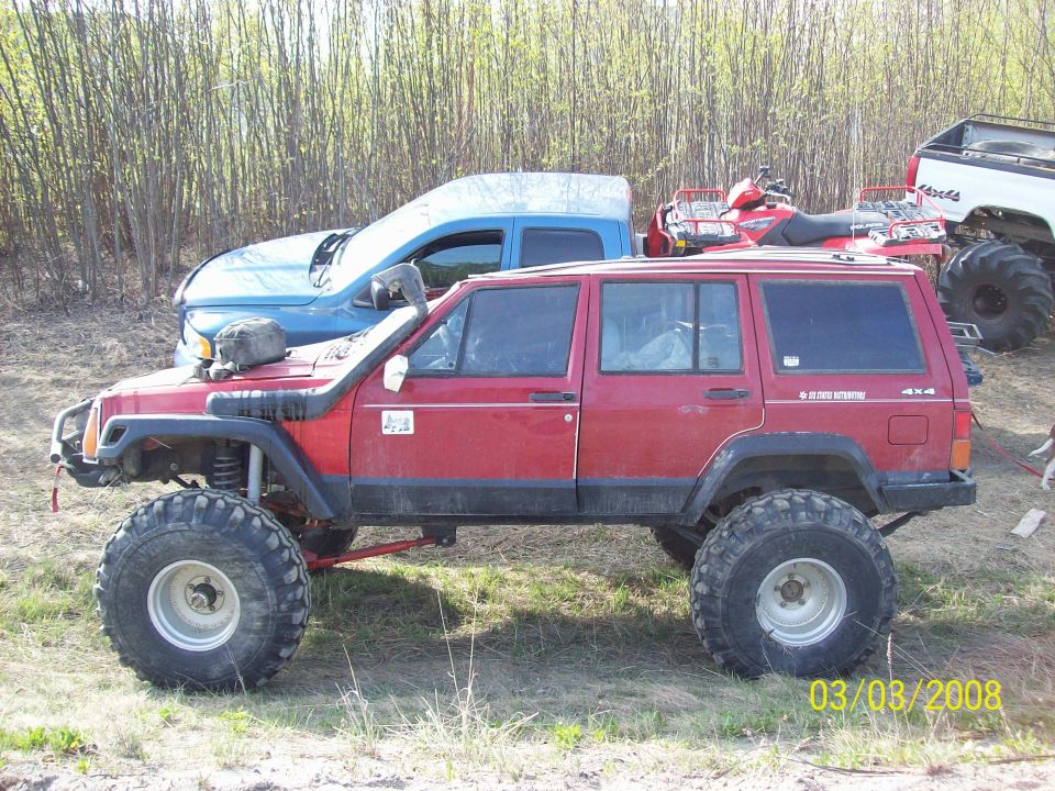 Red Jeep Cherokee XJ with snorkel, lifted suspension, and large tires parked on grass