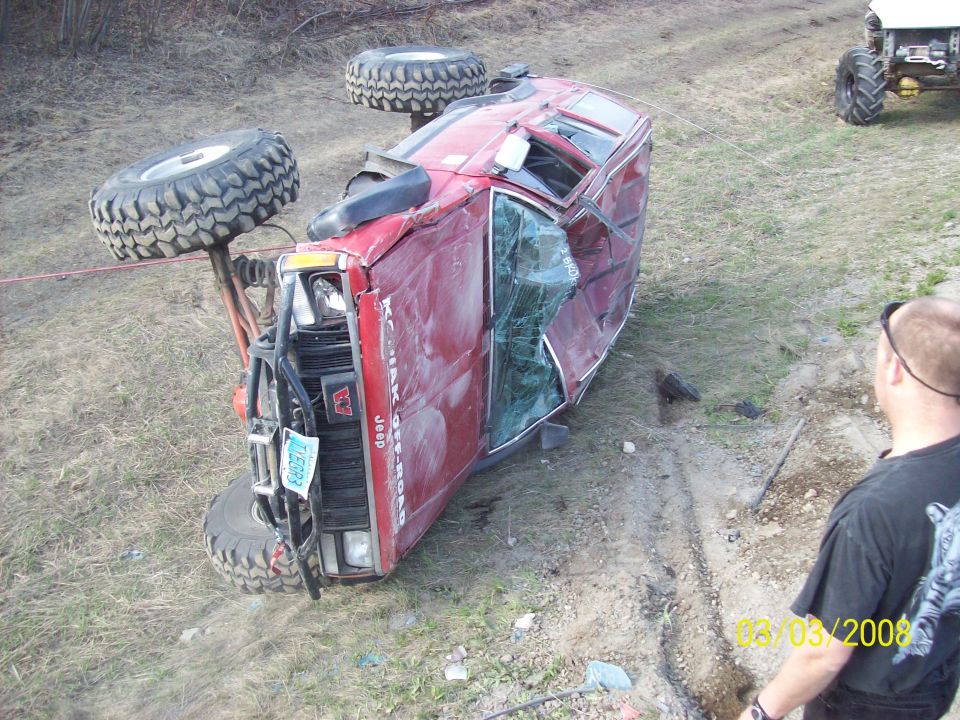 red Jeep rolled onto its side with a white tractor in the background