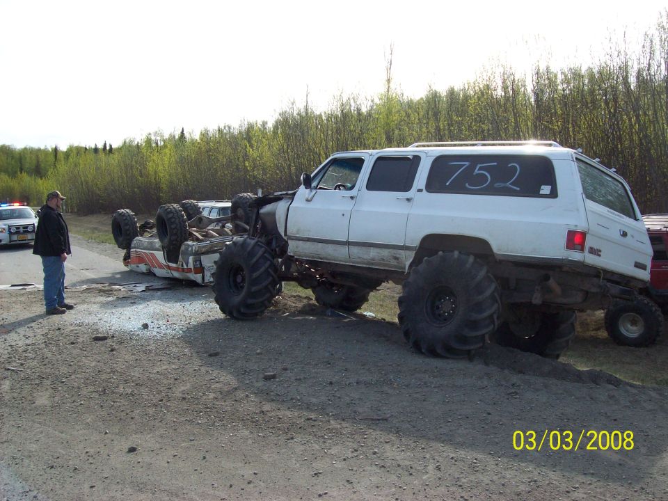 White monster truck next to an overturned vehicle. Police car and officer present. Number 752 on monster truck