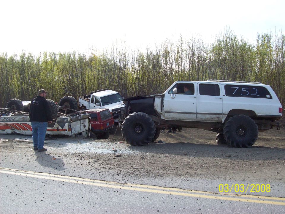 White SUV with oversized tires and number 752 on side, parked by overturned vehicles