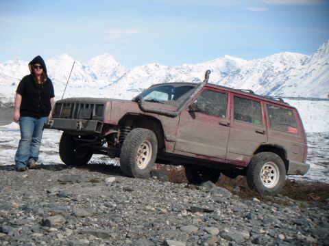 1998 Jeep Cherokee - A person poses next to a dirty Jeep Cherokee with a snorkel in a mountainous, snowy landscape.