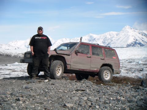1998 Jeep Cherokee - Man and his 1998 Jeep Cherokee parked on a rocky terrain with snow-capped mountains in the background.