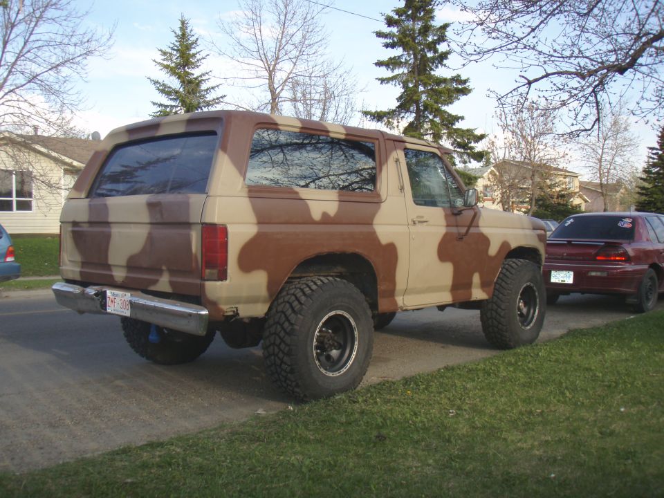 Camouflaged 1985 Ford Bronco, rear 3/4 view, lifted with off-road tires