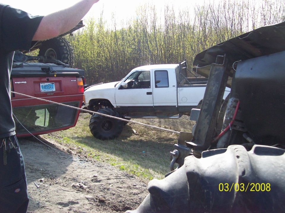 White pickup truck with oversized tires and a roll bar in the bed, parked next to a red SUV