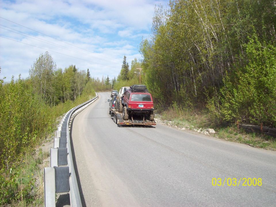 Red SUV on a trailer, rear view, with roof rack and spare tire