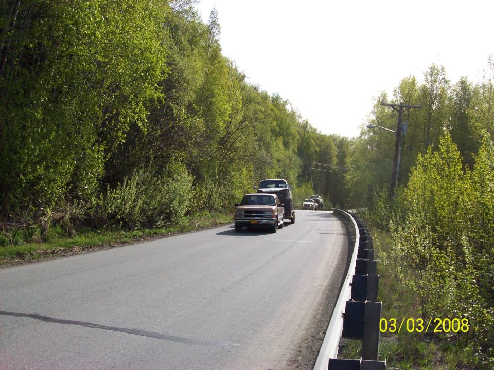 Pickup truck towing a trailer with a vehicle on it driving on a tree-lined road