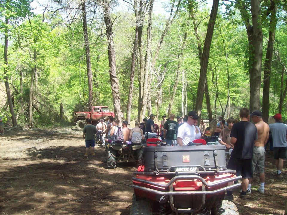 Group of people gathered in a wooded area with ATVs and a red pickup truck